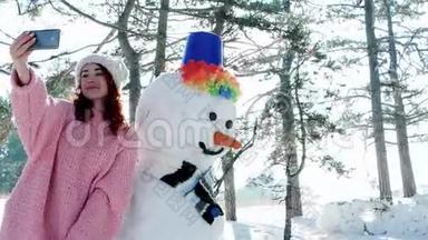 可爱的女孩和雪人合影，冬天的自拍，手机在手的一个年轻女人做有趣的自拍照片在里面。