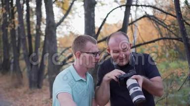 两个男人在大摄像机屏幕上看照片，说话和微笑。 森林背景。