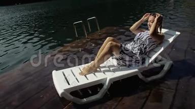 女人躺在太阳床上，戴着太阳镜和一条薄纱披肩。 女孩在洪水木水下码头休息。 路面是