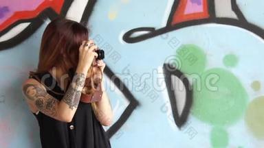 有<strong>纹身</strong>和老式相机的女孩站在<strong>涂鸦</strong>墙附近。