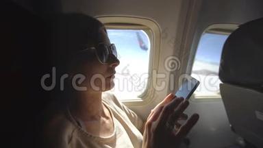 <strong>日</strong>落时分坐在飞机窗口附近的旅游妇女在飞行中使用<strong>手机</strong>