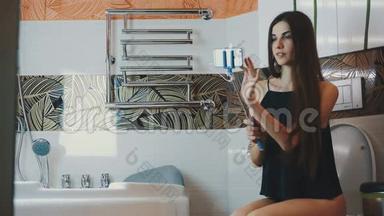 布鲁内特女孩<strong>坐</strong>在<strong>厕</strong>所在浴室持有智能手机蓝色莫诺波德。