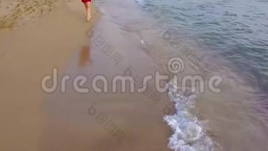 一个女人赤脚走在潮湿的沙滩上的俯视图。 海浪冲刷着沙滩上的脚印