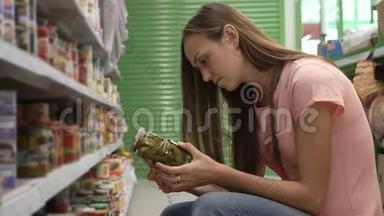 从<strong>超市货架</strong>上挑选罐头食品的女人读着标签