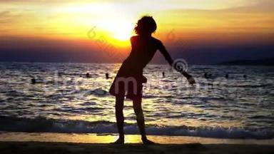 海洋日落背景下一个男孩的剪影，有趣的少年男孩在日落背景下跳舞