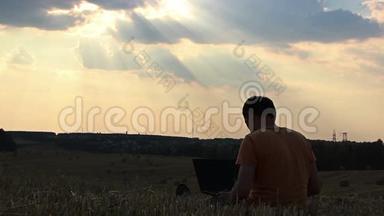 日落时分，一个人带着笔记本电脑在田野里，一个人在日落时分在上面工作