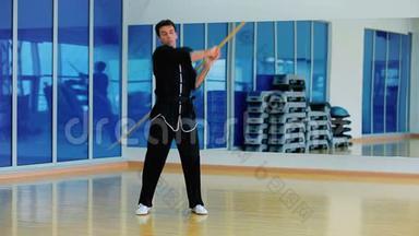 穿着黑色服装的主人在体育馆里用木棍训练打斗