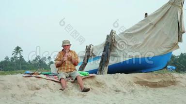 老人在渔船旁边的海滩上吹<strong>竹笛</strong>