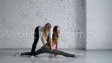瑜伽教练帮助女学生伸展腿部和做分裂