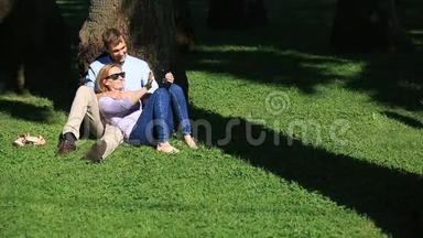 一对浪漫的情侣坐在棕榈树下。 一个女孩在一个男人的大腿上。 一对相爱的夫妇在草地上的公园里休息