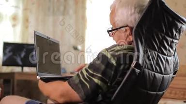 老人坐在靠近家庭<strong>电视</strong>的皮椅上，手提<strong>电脑</strong>。 带着<strong>电脑</strong>放松的男人
