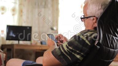 老人坐在电视机旁的皮椅上拿着电话。 男子打字短信和观看照片