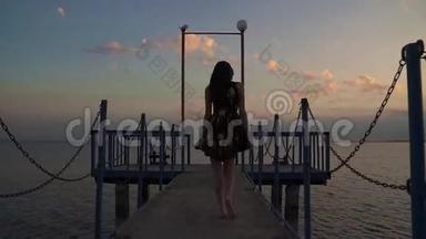 日落时穿着一件浅色衣服的漂亮<strong>女孩</strong>的<strong>剪影</strong>。 一个<strong>女孩</strong>正在海上走码头