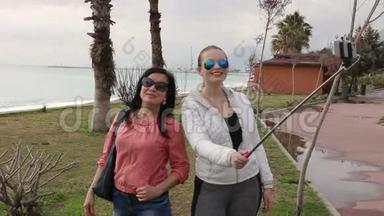 两名年轻女子使用智能手机手机相机在海滨拍摄自我肖像。