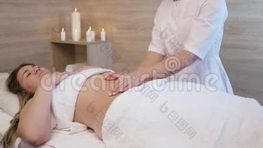 一位年轻女子在一家美容院做抗纤维素腹部按摩。 按摩师为年轻人做脂肪团按摩