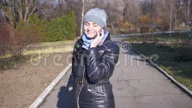 快乐的年轻女孩微笑着，慢动作地在城市公园的智能手机上交谈