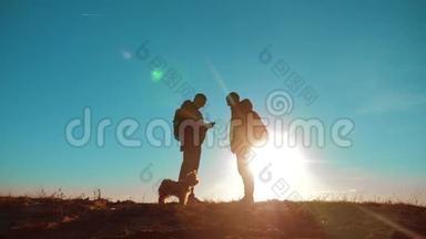 团队合作。 两名游客徒步旅行，男人和狗带着背包在日落时去徒步旅行。 慢动作视频。 智能手机