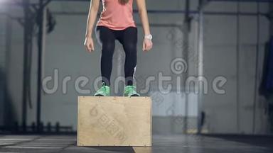 年轻的强壮的女人，穿着运动服，在健身房做一套<strong>盒子</strong>跳跃。 女孩跳到<strong>木头</strong>上