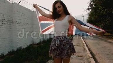 微笑的少女用大彩旗在风中编织，复古的色彩拍摄。 站在墙边的年轻女子