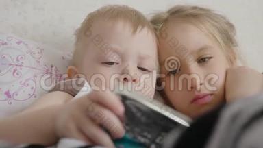 可爱的弟弟妹妹使用数字平板电脑，微笑着，看上去很开心。 兄弟姐妹玩得开心