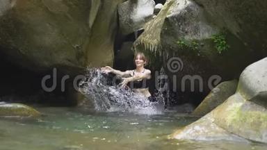 在绿色的热带森林中，美丽的女孩用手在山间湖泊中<strong>溅起水</strong>花，小瀑布和