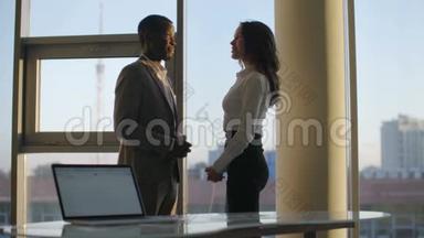 两位公司员工在大全景窗前相互交谈的剪影.. 城市天际线背景