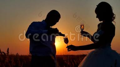 一对夫妇欣赏香槟酒的剪影。 浪漫的情侣在大自然阳光下剪影日落