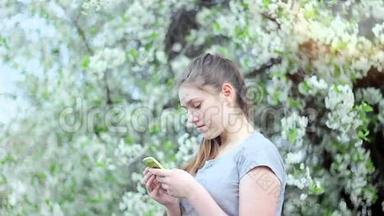 公园里有智能<strong>手机</strong>的少女。 <strong>春天</strong>。 在一棵开花的树的背景下