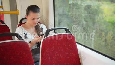 年轻女孩在乘坐公共汽车<strong>时使用</strong>智能手机，美丽的女人在城市交通中<strong>使用</strong>她的手机