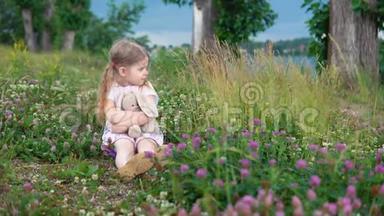 一个小女孩和一只玩具兔子在草地上的<strong>四叶草</strong>中玩耍