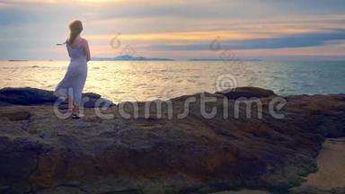 年轻女子走在岩石上，欣赏日落美景，溅起浪花