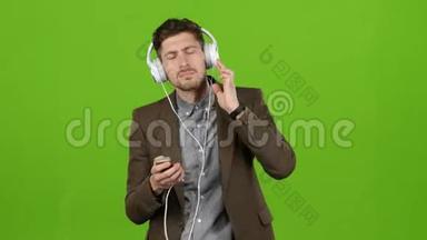 男人通过耳机听音乐，跳舞和唱歌。 绿色屏幕