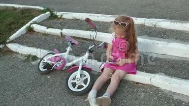 一个穿着粉红色裙子的小女孩坐在台阶上的公园里，戴着耳机享受着智能手机。