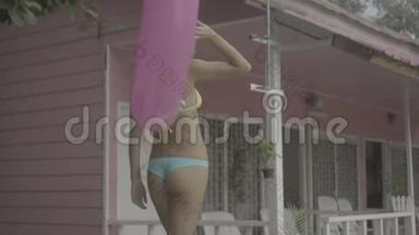 穿着比基尼戴着太阳镜、带着粉色充气戒指走着的漂亮年轻快乐的女人，在粉色房子的背景下被隔离开来