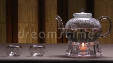 美丽的温暖图片透明茶壶水壶与美味的绿红茶在桌子上与蜡烛。 玻璃水壶