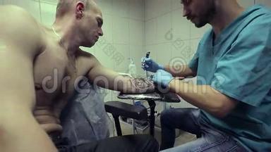 纹身艺术家在工作。 男人画在他手臂上的女人的脸上。 快关门。 纹身沙龙