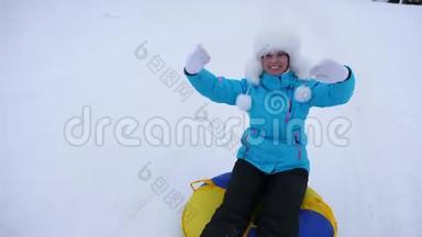 美丽的年轻女子在雪地里滑过充气的雪管和波浪手。 快乐的女孩滑过雪地