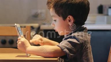 端口：一个可爱的孩子使用平板电脑在家里的一张桌子。 休闲服。 侧视图