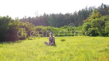 幸福的年轻女子坐在风景名胜区的绿色草坪上，背景是夕阳。