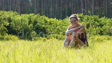 幸福的年轻女子坐在<strong>风景名胜</strong>区的绿色草坪上，背景是夕阳。