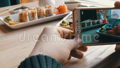 青少年的手在智能<strong>手机</strong>上<strong>制作</strong>食物的照片。 背景上日本料理的寿司卷