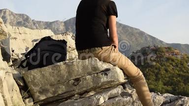 年轻的金发女郎坐在山崖边上，与美丽的山峰相映成趣
