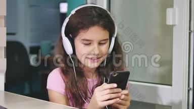 带着耳机坐着玩智能手机的少女。 女生在室内智能手机上玩网络游戏