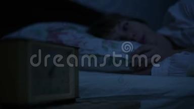 一个穿<strong>睡</strong>衣的女孩躺在床上，看<strong>着</strong>闹钟<strong>睡不着</strong>。 从小时到小时的可变焦点