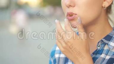 女孩在街上在户外吃薯片。 漂亮的年轻女人吃薯片。