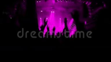 一个激动的人群在摇滚音乐会上鼓掌和跳跃的慢动作视频。 粉色舞台灯光照亮<strong>会场</strong>..