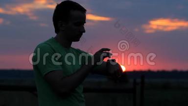 一个人在日落时看并触摸智能<strong>手表</strong>。 美丽的红天和树林后面的太阳