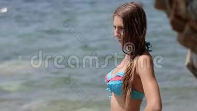 一位留着长发和比基尼的年轻女士站在岩石海滩上摆姿势