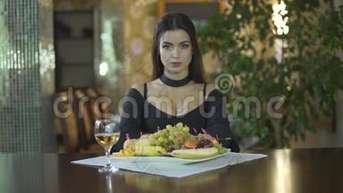 年轻迷人的黑发女人，穿着黑色连衣裙，乳沟，独自吃水果，葡萄，一个人在<strong>高档</strong>餐厅吃饭