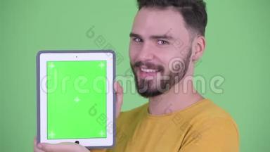 年轻英俊的大胡子男子脸上挂着数码平板电脑